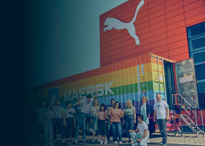 A group of smiling people in front of the rainbow container.