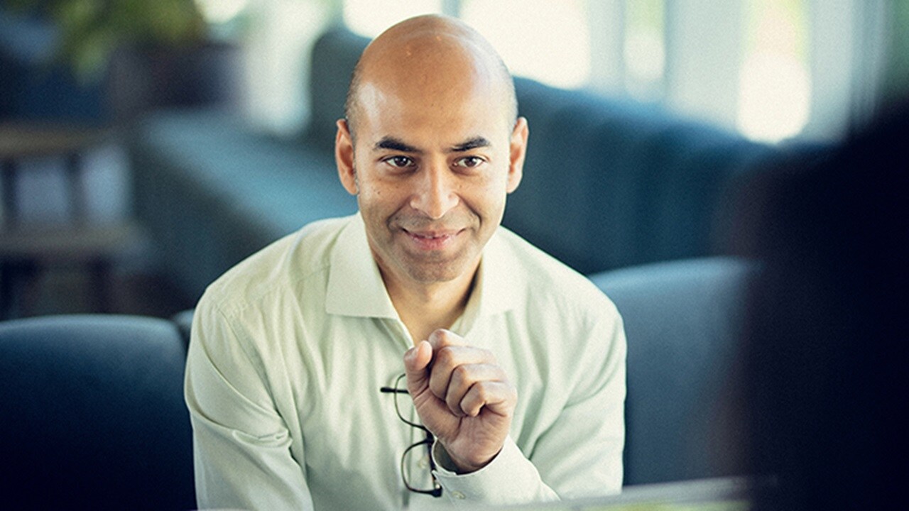 A cyber security professional smiling and is seated on a sofa.