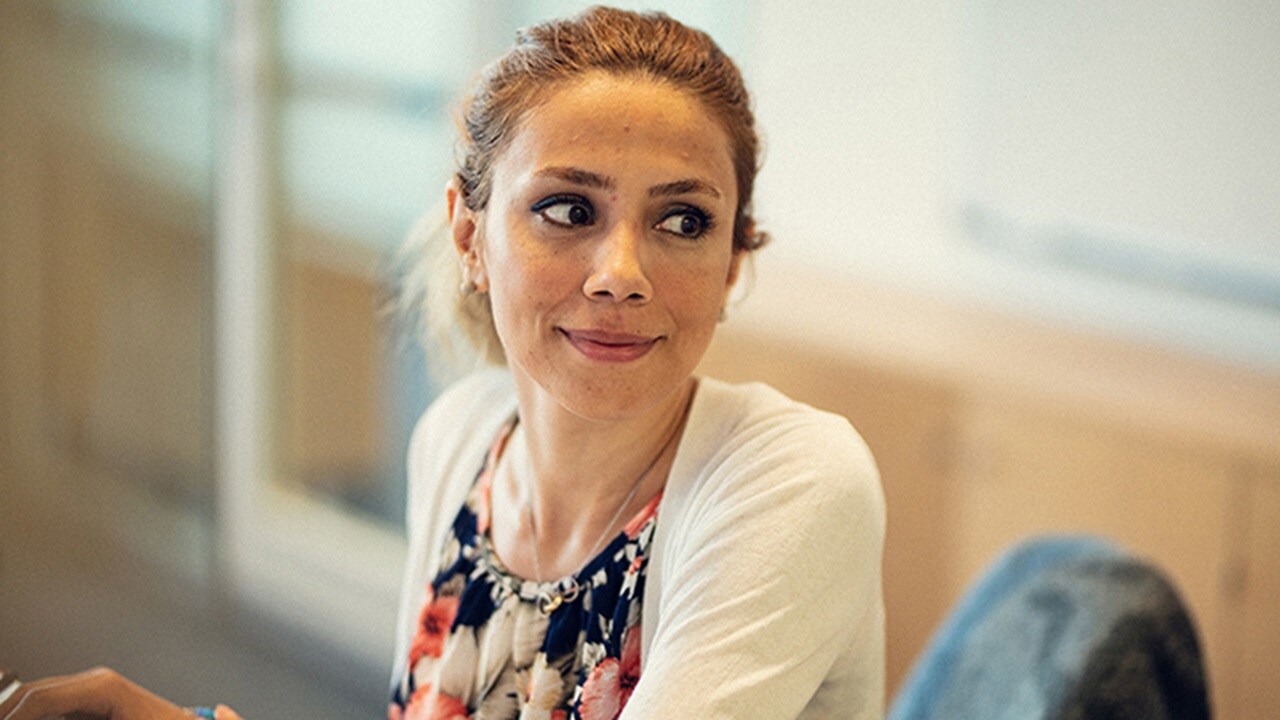 一位女性 UX 設計員工坐在自己的工作站上，她面帶微笑，而且看向左邊。