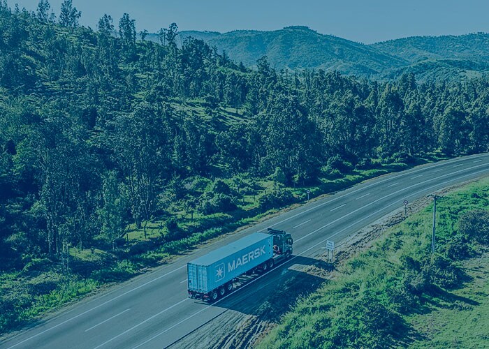 Maersk truck driving along a scenic highway surrounded by green hills and forested landscape