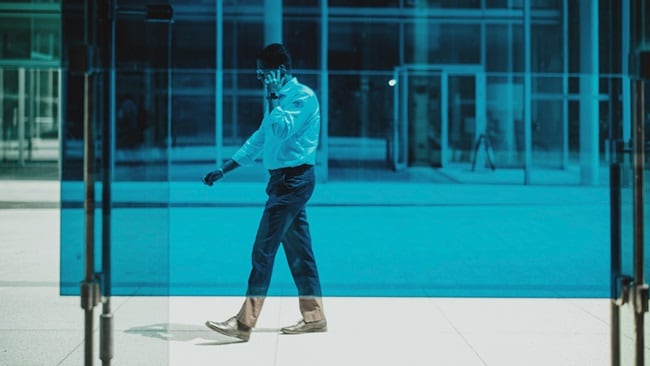 A man talking on his phone while walking behind a blue glass