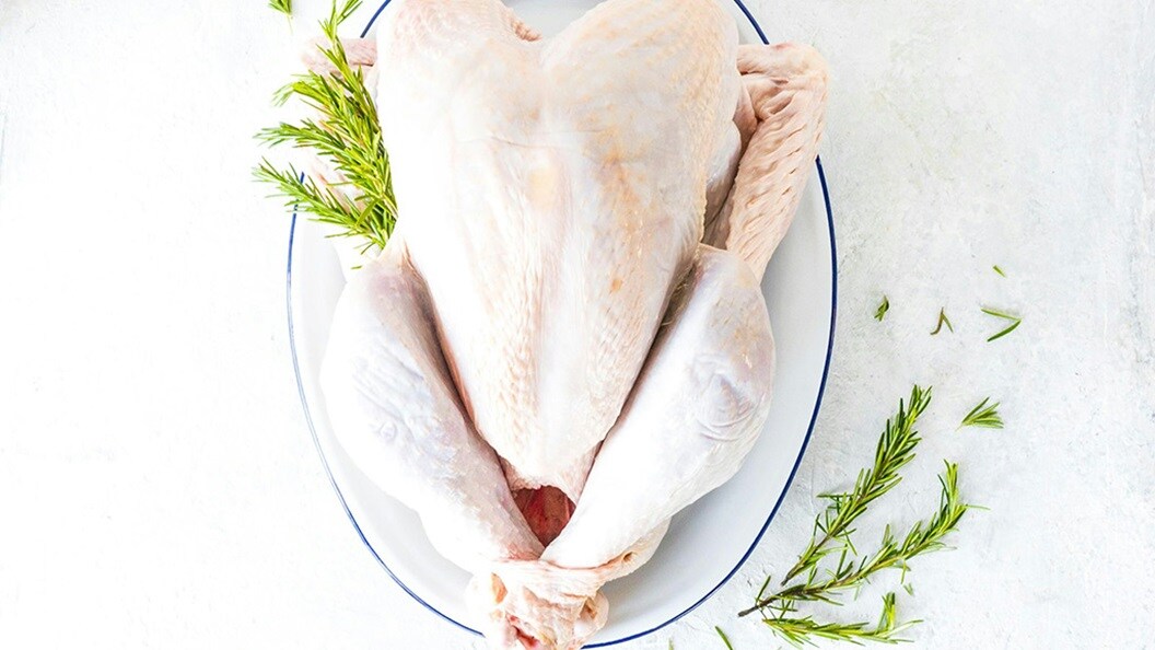 a whole chicken on a plate with a sprig of rosemary