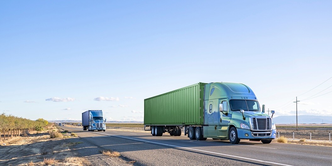 Two large trucks traveling down a highway.