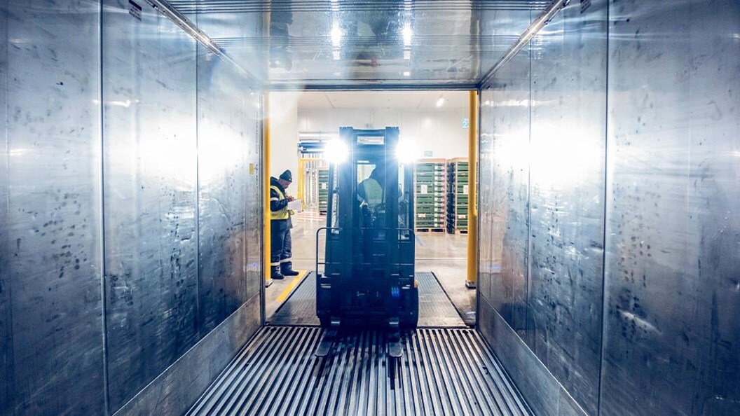 A forklift enters a container box and flashes its lights into it.