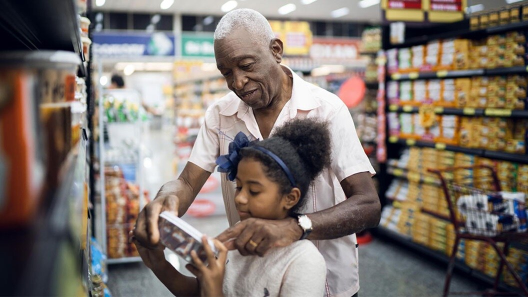 An elderly man helping a young girl read a product label while grocery shopping in a supermarket