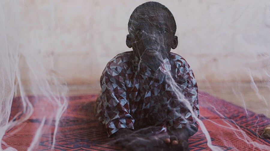 Preventing Malaria - An African kid lying on a mat and seeing through the mosquito net.