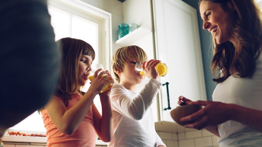 Mother smiling at her two kids who are drinking a glass of juice
