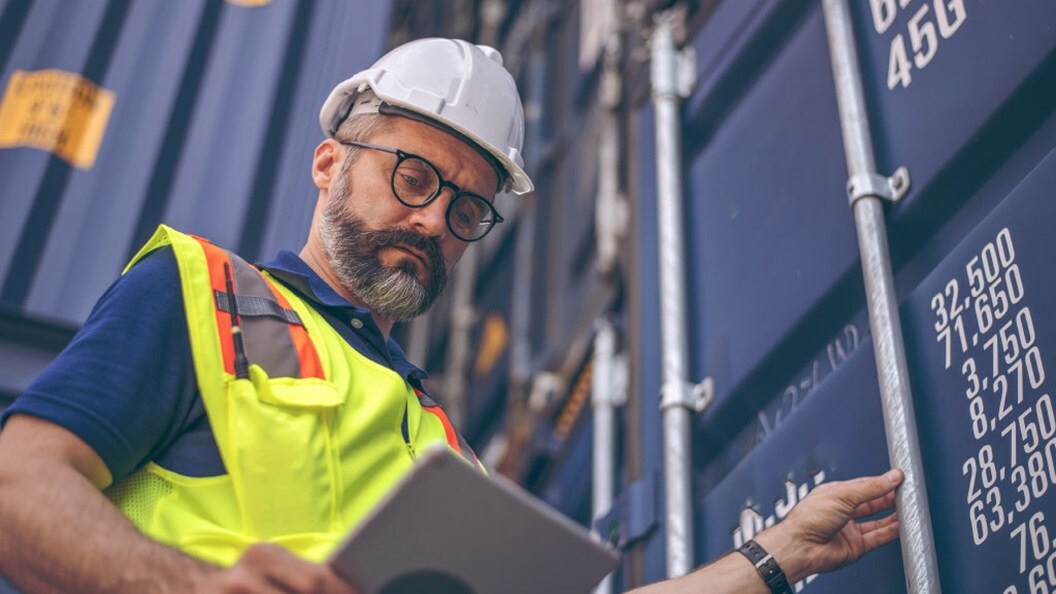 A worker looking at a tab standing next to a container