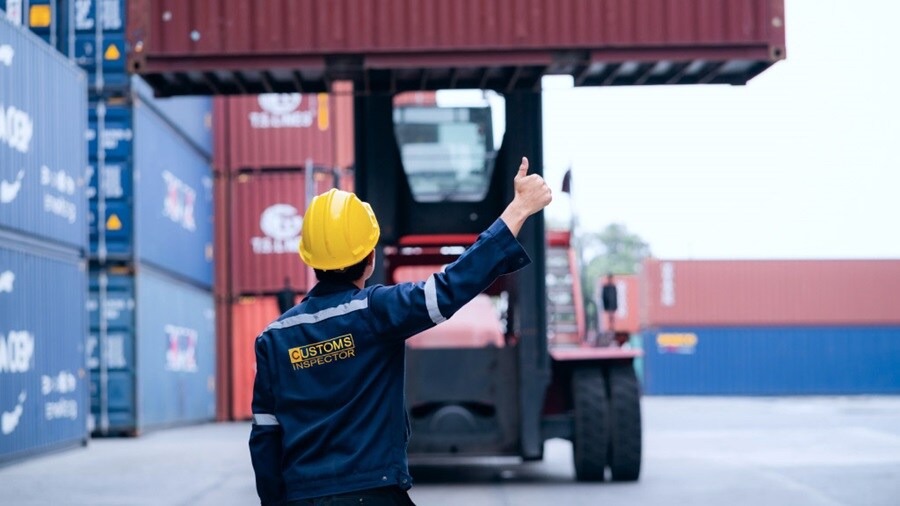 A man wearing a hard hat points towards a forklift, indicating its location or operation on a construction site.