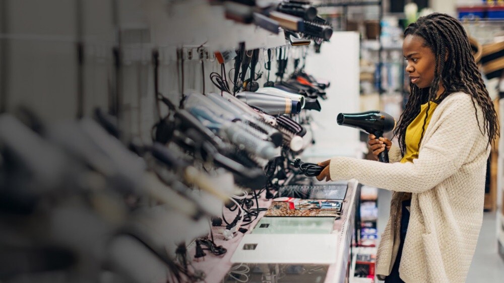 A woman is browsing a hair dryer in a store, considering her purchase.