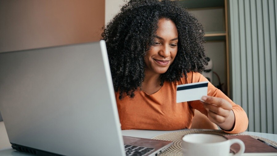 A woman with afro hair shops online, using a laptop and a credit card for her purchase.