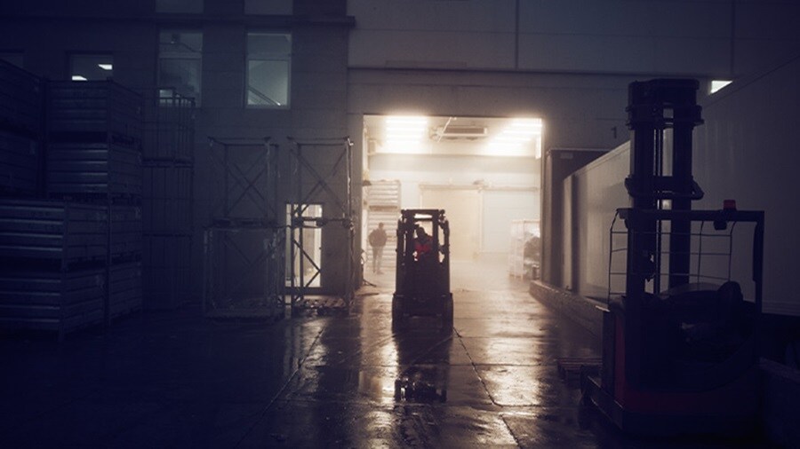 Forklifts operate in a dimly lit warehouse with mist and reflective wet floors.