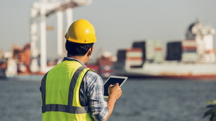 A man wearing a hard hat and safety vest is focused on a tablet computer in a construction setting.