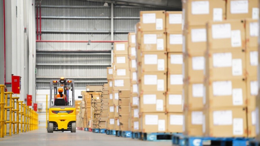 A forklift truck navigates through a spacious warehouse, transporting goods between shelves.