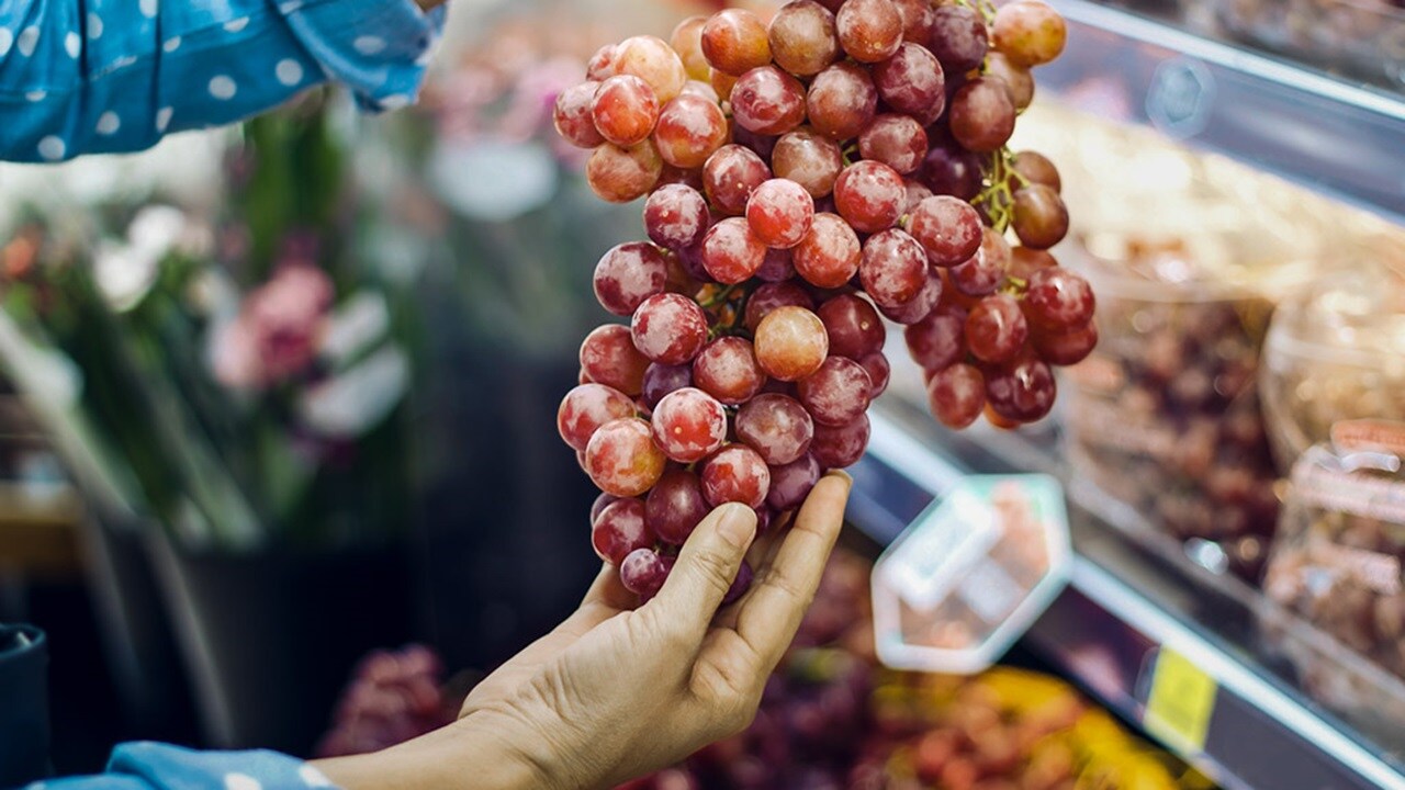 Woman choosing bunch fresh red grape to buy in Supermarket