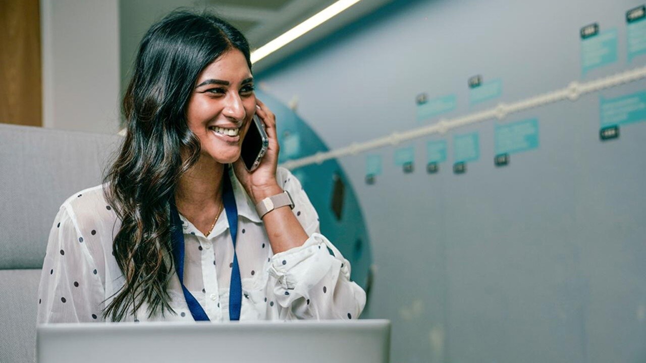 Woman sitting in an office talking on the phone and smiling.