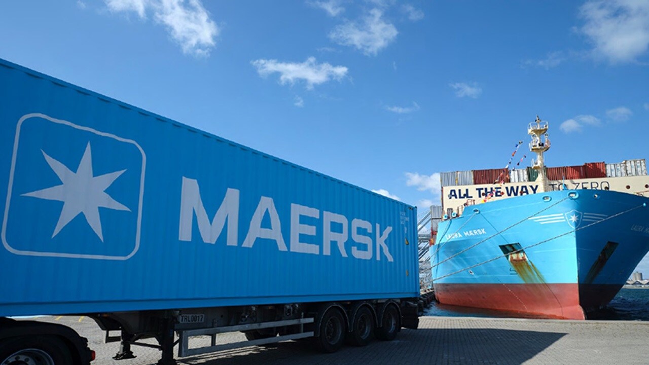 A Maersk shipping container truck at a busy port under a clear blue sky.