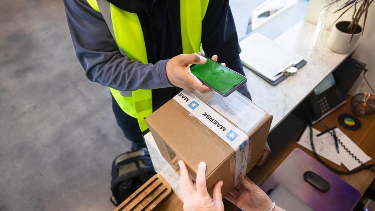 A delivery worker in a high-vis vest handing over a Maersk-branded parcel to a customer.