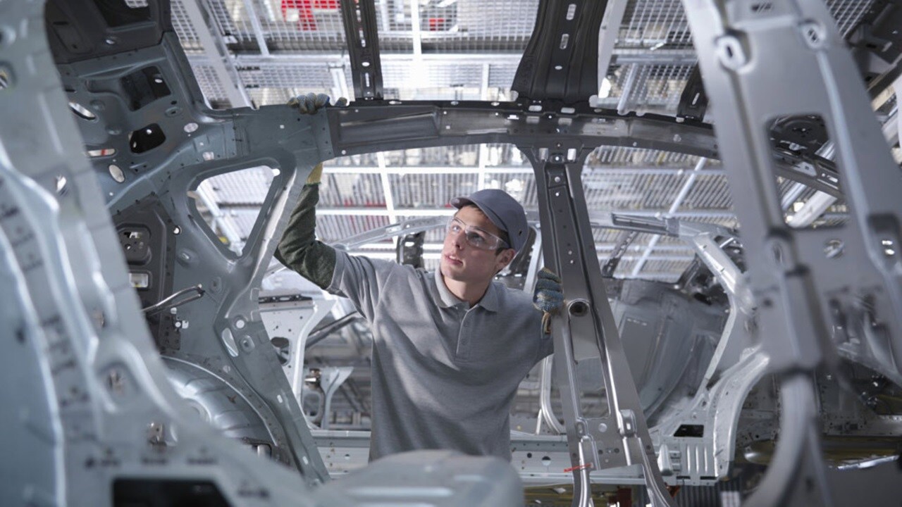 A factory scene showing a man working on a car, surrounded by tools and automotive equipment.