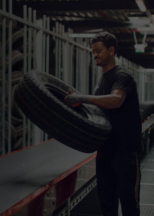 A man holds a tire in a spacious warehouse filled with shelves and equipment.