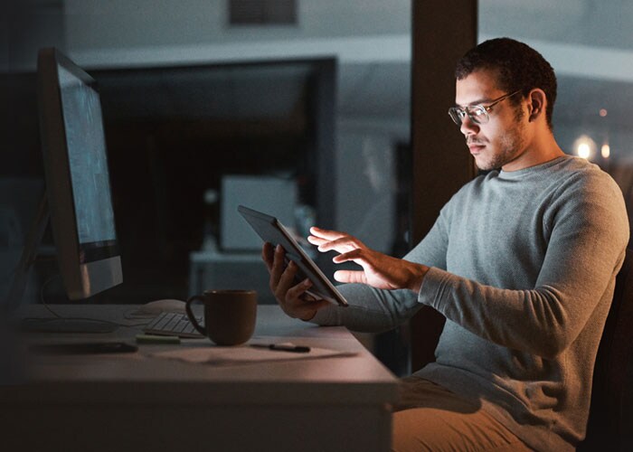 A man with glasses seated at their workstation and using a tablet to explore digital solutions.