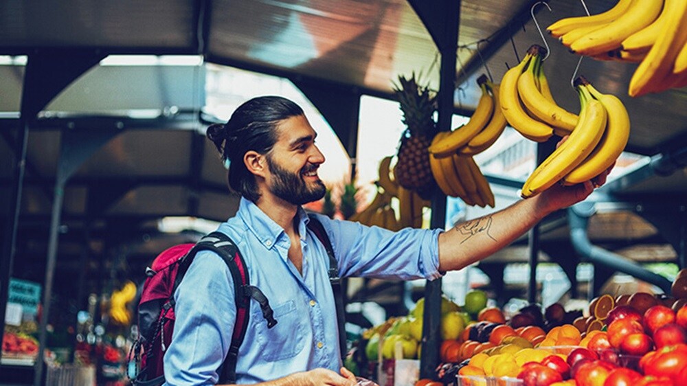Un hombre sonriente mirando plátanos en un mercado de frutas.