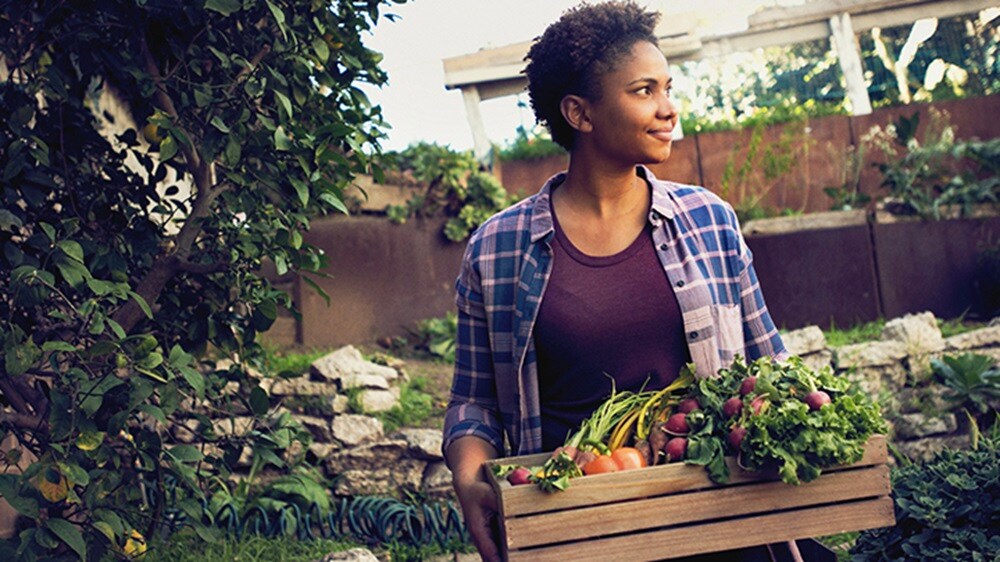 Carga perecedera - Una mujer sonriente sosteniendo una cesta de frutas y verduras.