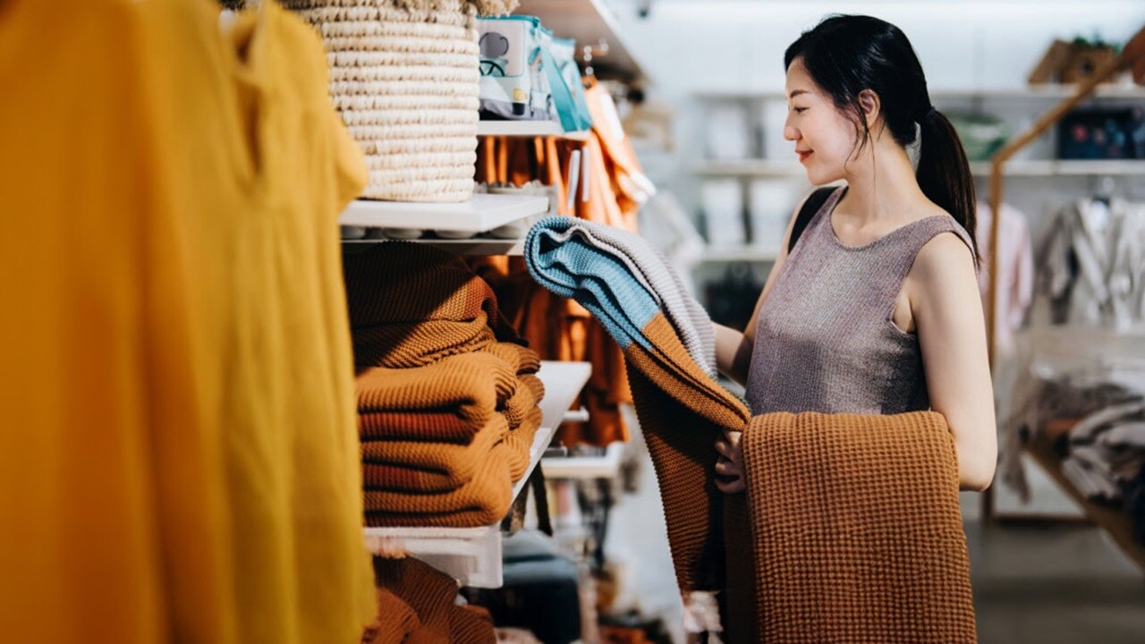A woman browsing clothes in a store, thoughtfully assessing garments on the racks.