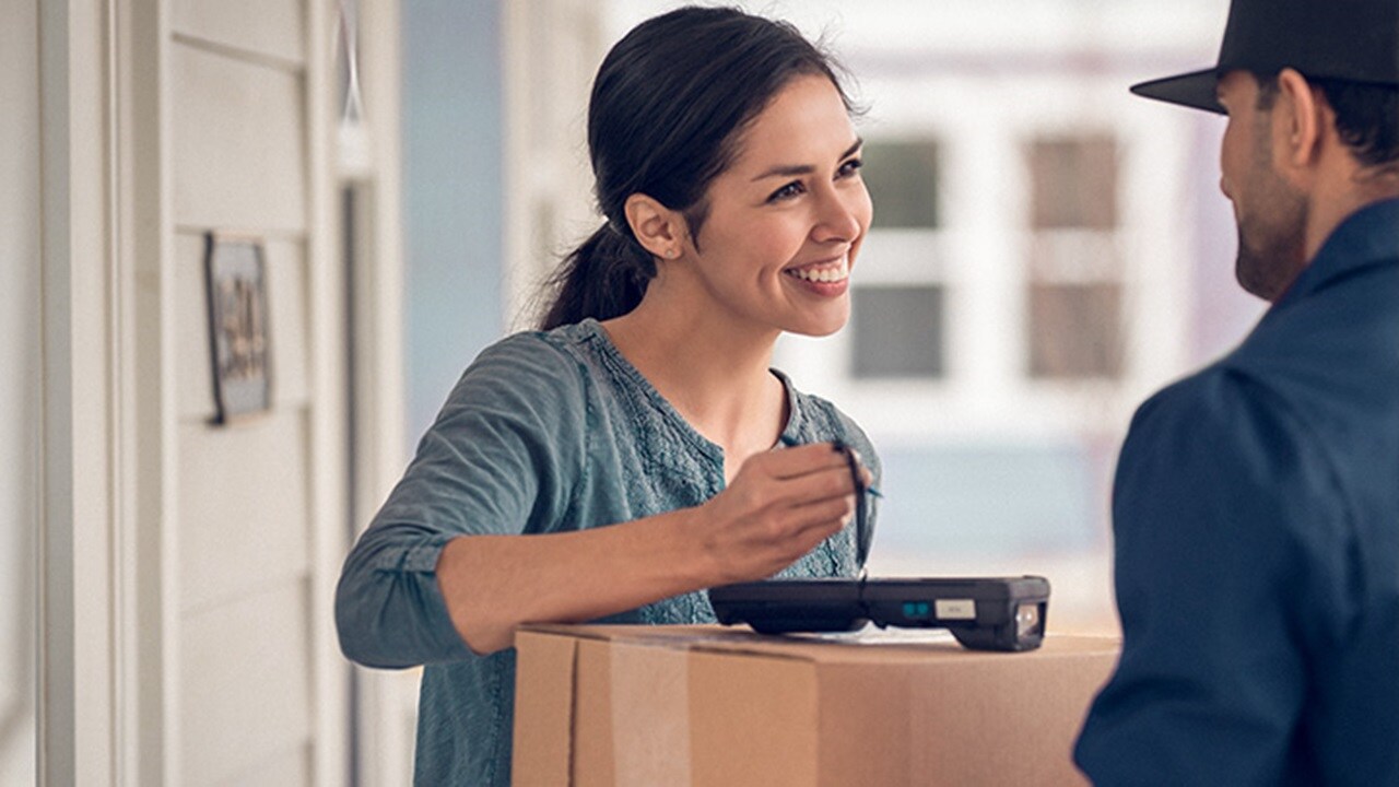 Parcel delivery - A smiling woman receiving a package from a delivery guy and signing the receipt.