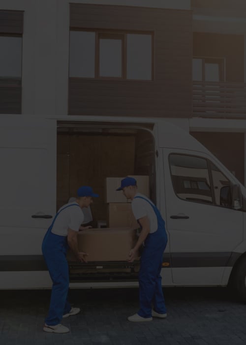 Two logistics workers unloading boxes from a delivery van in front of a modern residential building, representing efficient last-mile delivery services.