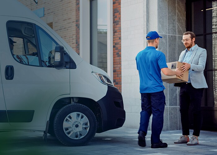 Consegna di e-commerce nell’ultimo miglio – Addetto alle consegne che consegna un pacco a un cliente. Alle sue spalle, un furgone con pacchi.