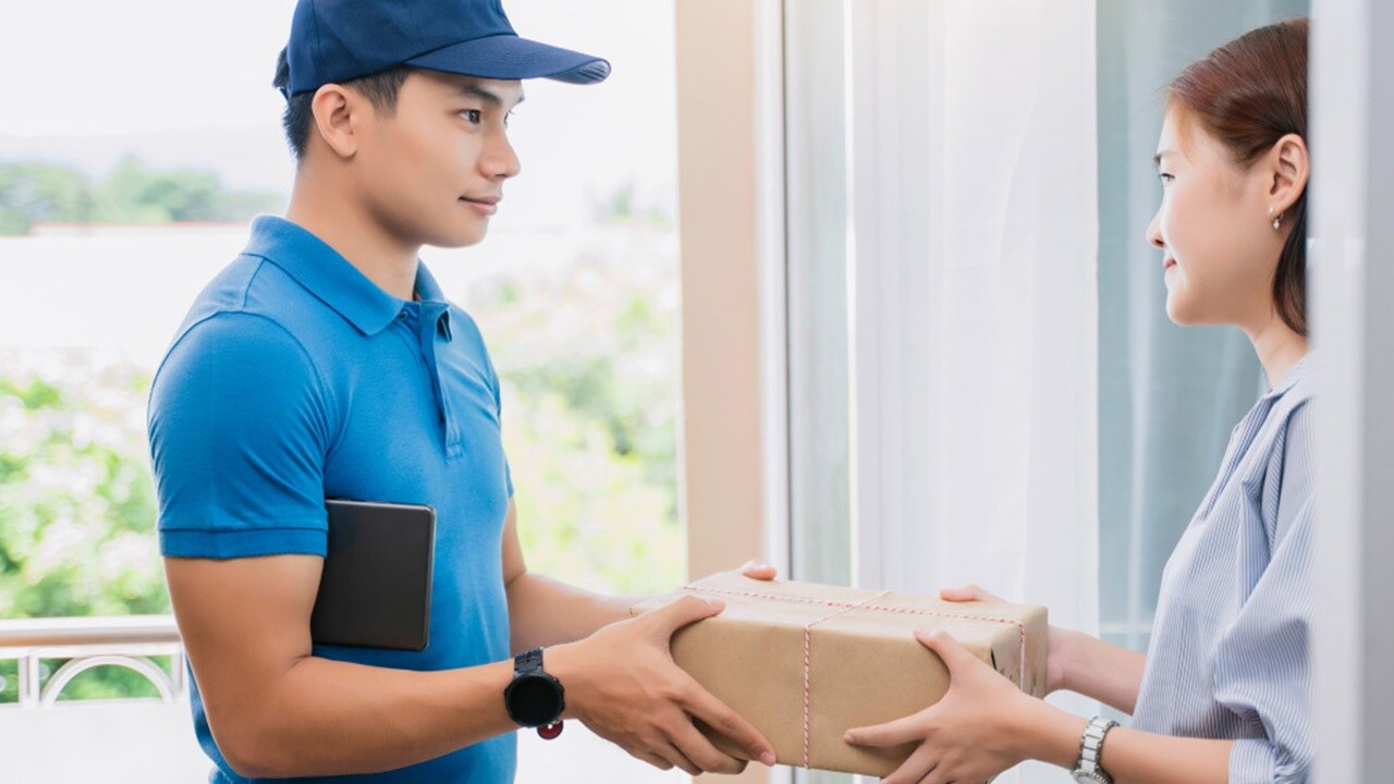 自宅で笑顔のお客様に荷物を引き渡す配送業者。ラストマイルロジスティクスと顧客満足度を表す