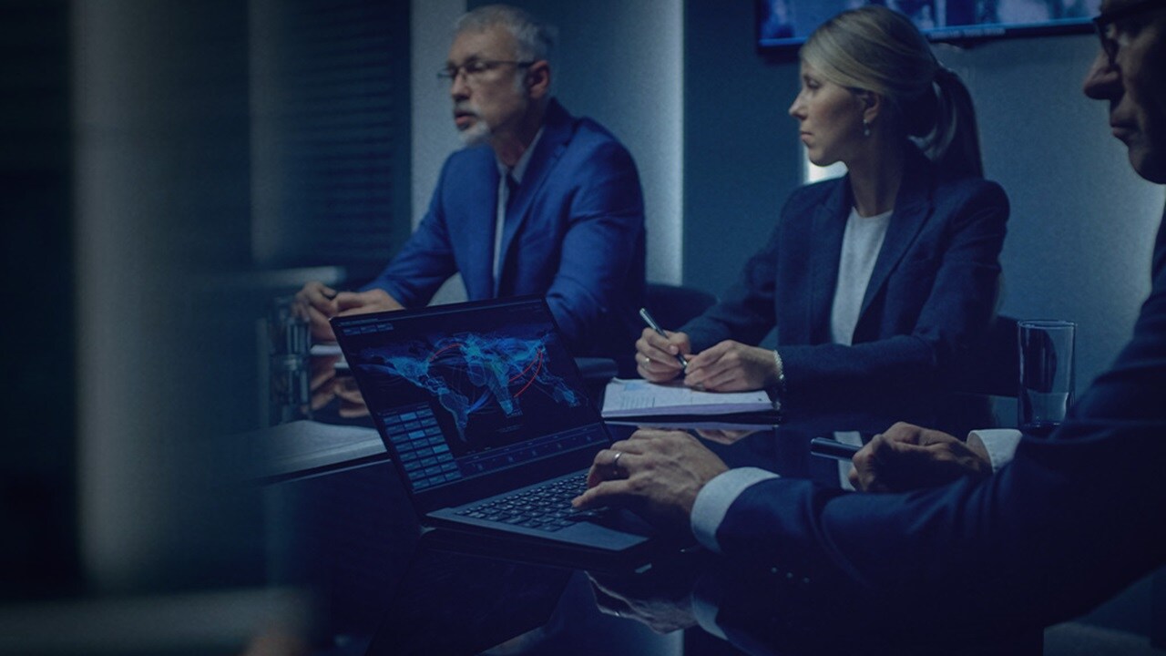 A group of business professionals in a dimly lit conference room, engaged in a serious discussion.