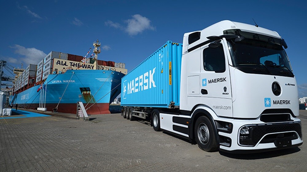 Maersk electric truck with container parked near the cargo ship Laura Maersk at a port, showcasing sustainable intermodal transport