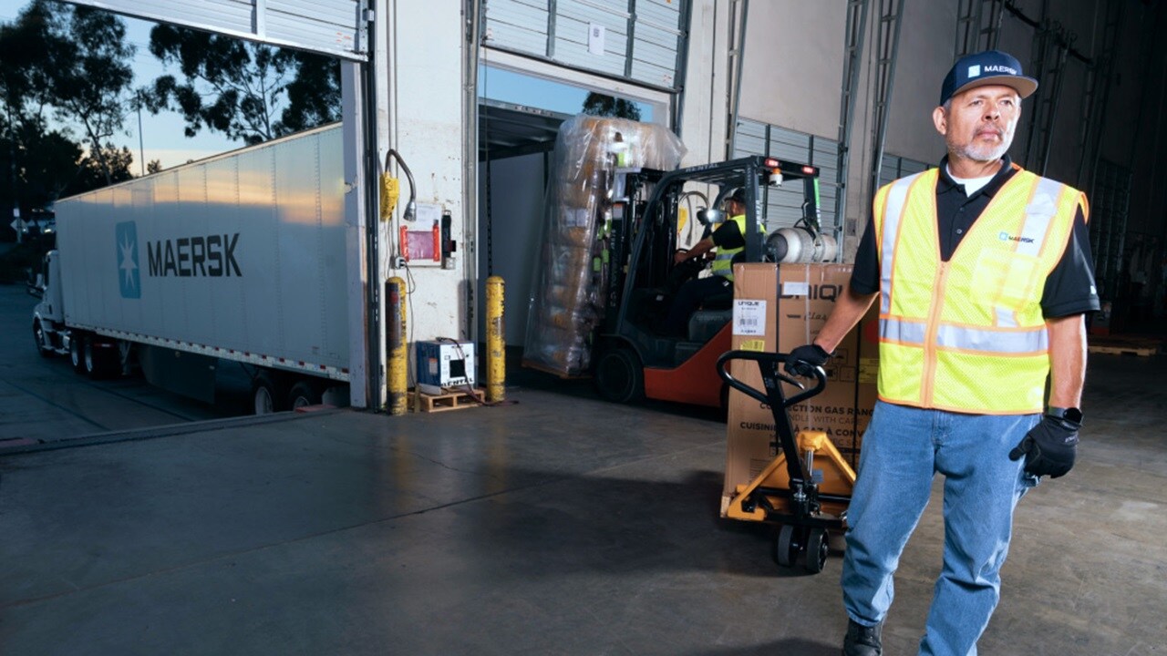 지게차를 운전하는 창고 작업자가 목재 팔렛 위의 상자를 Maersk 컨테이너 트럭에 적재.