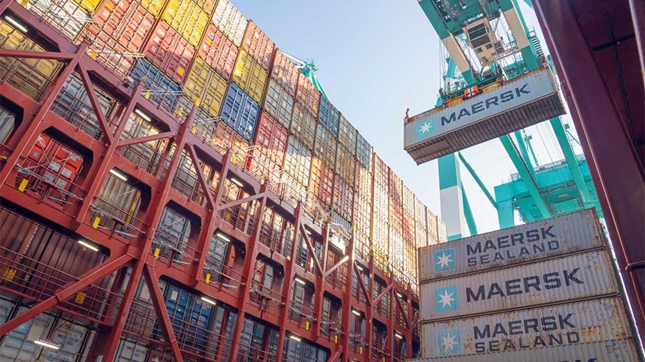 Shipping containers being loaded onto a container vessel at a port terminal using quay cranes as part of global ocean freight operations.